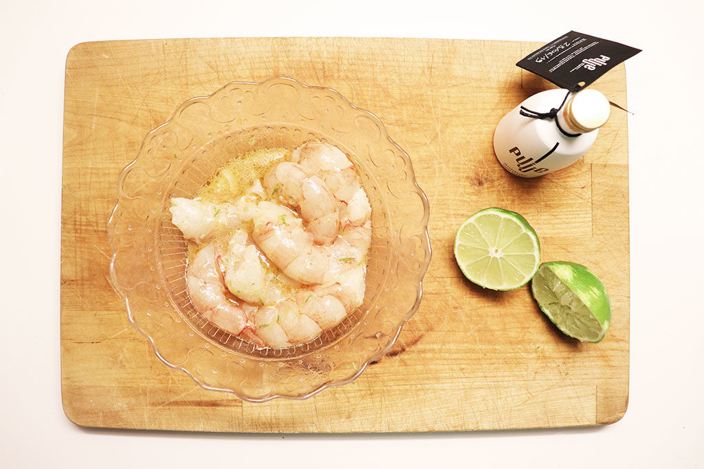 foto di un tagliere con una ciotola di vetro con gamberi e un lime tagliato a metà