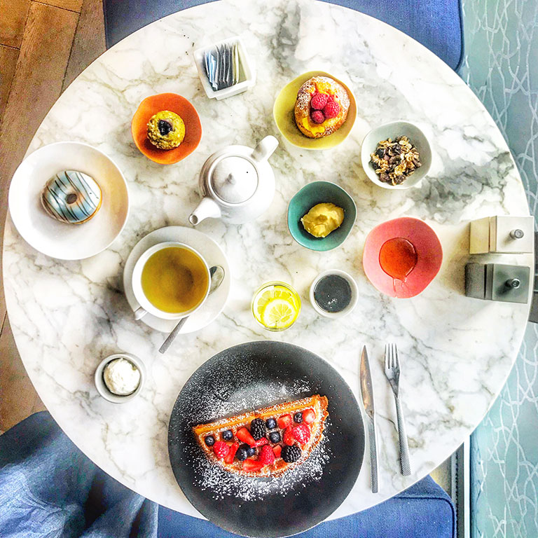 foto di un tavolo rotondo in marmo con la colazione di waffel succhi di frutta tè e pasticceria