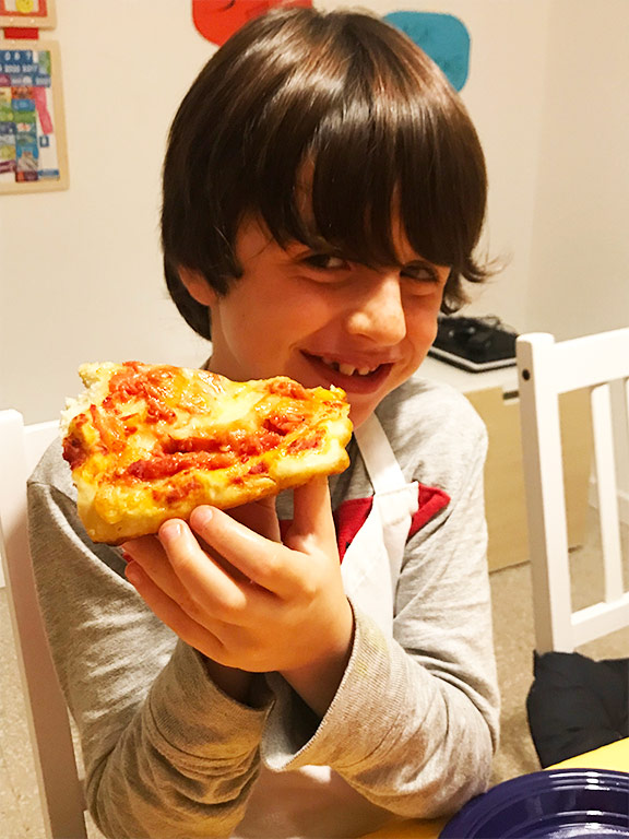 foto di un bambino che mangia la pizza rossa mentre sorride